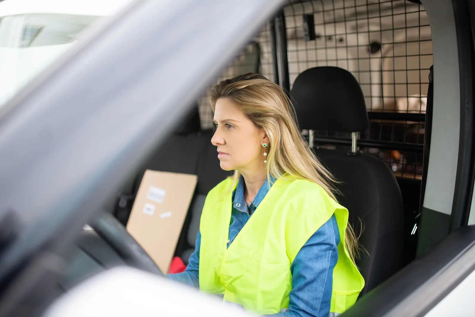 Caucasian female courier delivering packages in a van, wearing a safety vest. The compliance side of a local delivery business