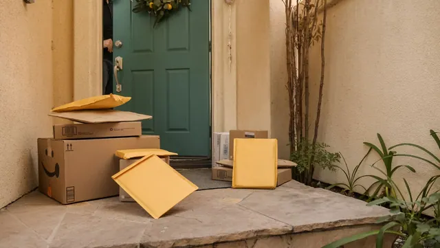 Multiple delivery packages and parcels stacked at a teal front door entrance on a porch. Local delivery services and packages guide for 2027
