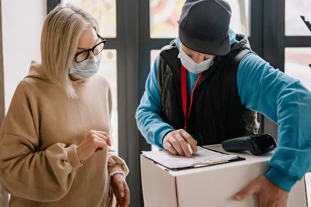Elderly woman receives a parcel from delivery man wearing masks, highlighting contactless service indoors. Medical courier HIPAA compliance for local delivery businesses