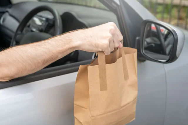 An image of a paper takeout bag being handed out of a car window by a delivery driver. The bag is weighed down a little by its contents. This image is free to use under the Creative Commons Attribution Licence. If you use it, please throw in a link back to us at meanwell-packaging.co.uk/. Sales tax on delivery fees by state: six-state overview